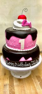 Custom three-tier pink and chocolate first birthday cake with fondant decorations, Mia's Brooklyn Bakery NYC