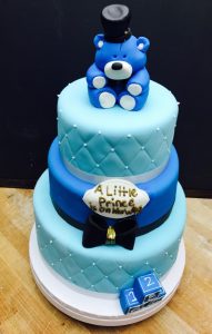 Custom three-tier blue baby shower cake with teddy bear topper and "A Little Prince Is On His Way" decoration, Mia's Brooklyn Bakery NYC