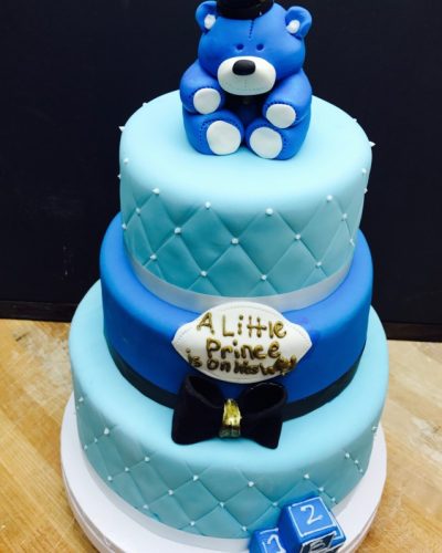 Custom three-tier blue baby shower cake with teddy bear topper and "A Little Prince Is On His Way" decoration, Mia's Brooklyn Bakery NYC
