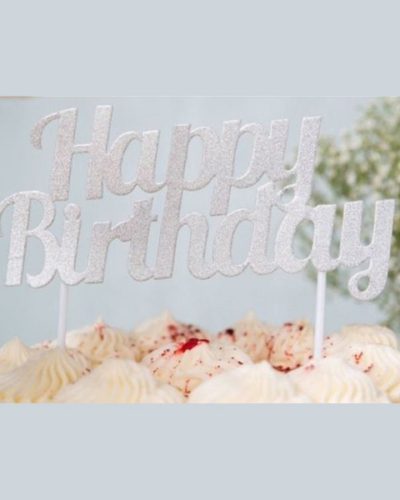 Silver happy birthday cake topper with elegant script lettering displayed on vanilla frosted birthday cake with colorful sprinkles