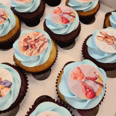 Set of chocolate edible image cupcakes featuring adorable baby portraits and milestone photos printed on round white fondant toppers. These custom photo cupcakes from Mia's Bakery are decorated with light blue buttercream frosting and showcase various baby pictures including newborn poses and first birthday moments. Perfect for baby showers, first birthdays, and milestone celebrations using edible image printing technology on cupcakes.