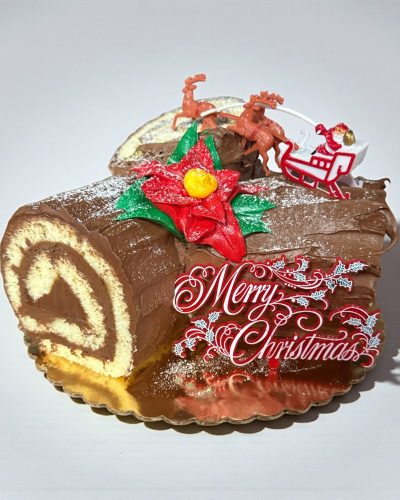 Chocolate yule log cake with “Merry Christmas” decoration, Santa sleigh and reindeer topper, and festive holiday design.